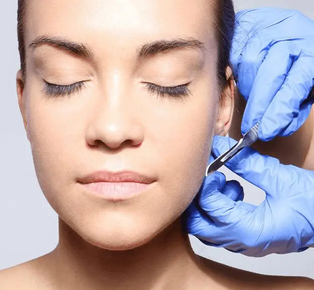 A person with closed eyes receives a facial treatment with a small tool, administered by gloved hands.